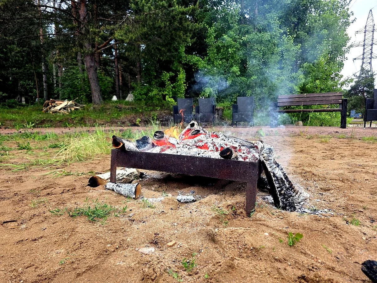 Костровая чаша с углями и лёгким дымом на лесной площадке